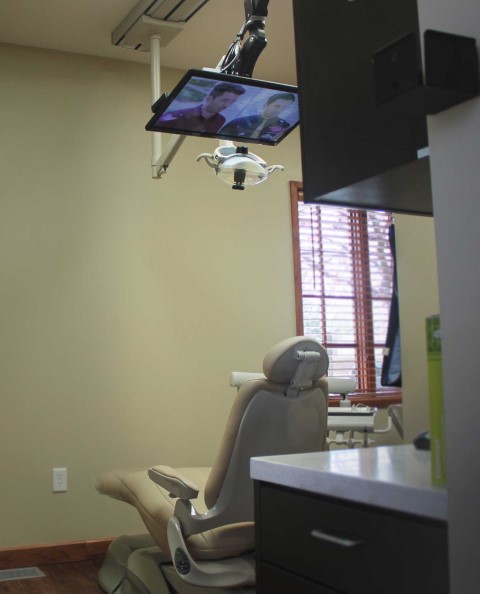 Photo looking into a dental office where a patient chair is below a digital TV they watch during a procedure