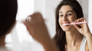 Photo of young woman looking in bathroom mirror while brushing her teeth